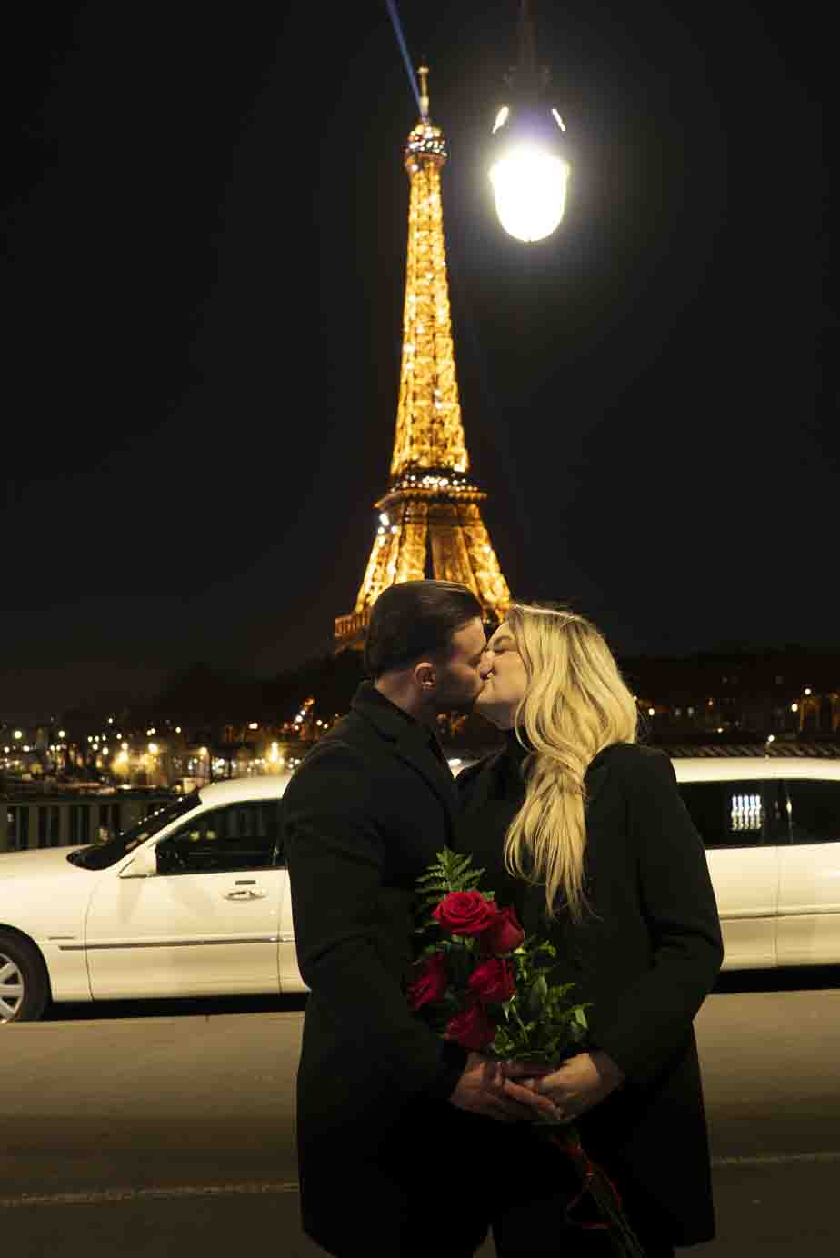 marriage proposal Romantic photo session in Paris: a couple embracing on the Bir-Hakeim bridge with the illuminated Eiffel Tower in the background, a limousine and holding a bouquet of roses.