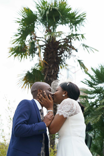 Photographe mariage Paris 13e – Mariés s'embrassant devant un palmier sur le parvis de la mairie, capturé par un photographe professionnel