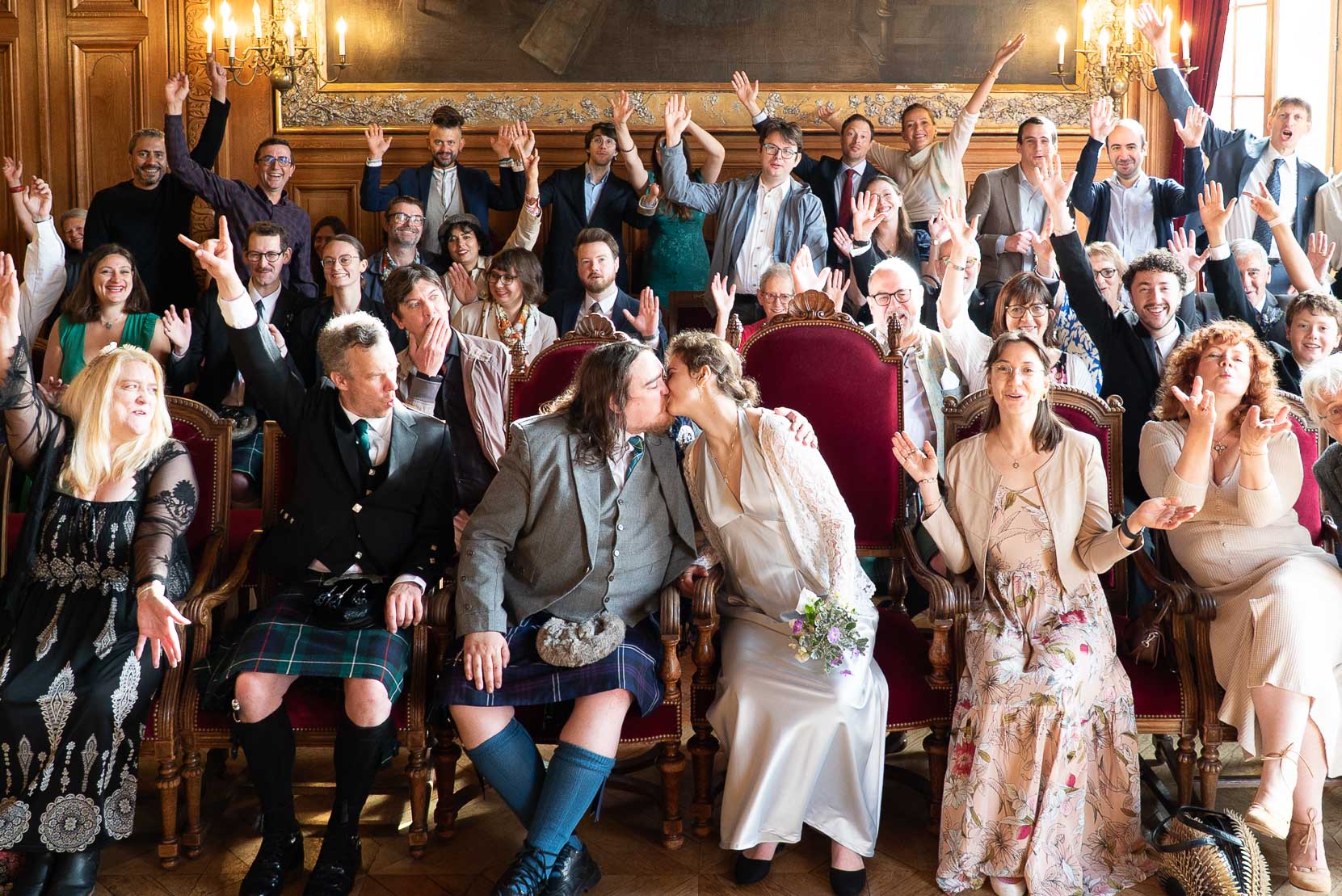 Photo de groupe joyeuse devant la mairie du 19e — baiser des mariés entourés de leurs proches, séance photo mariage paris