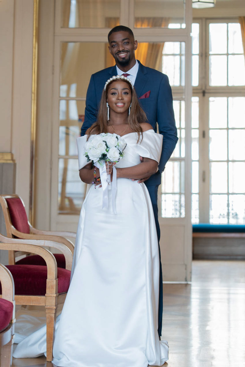 Le couple de mariés posant avec le bouquet devant la mairie de Paris