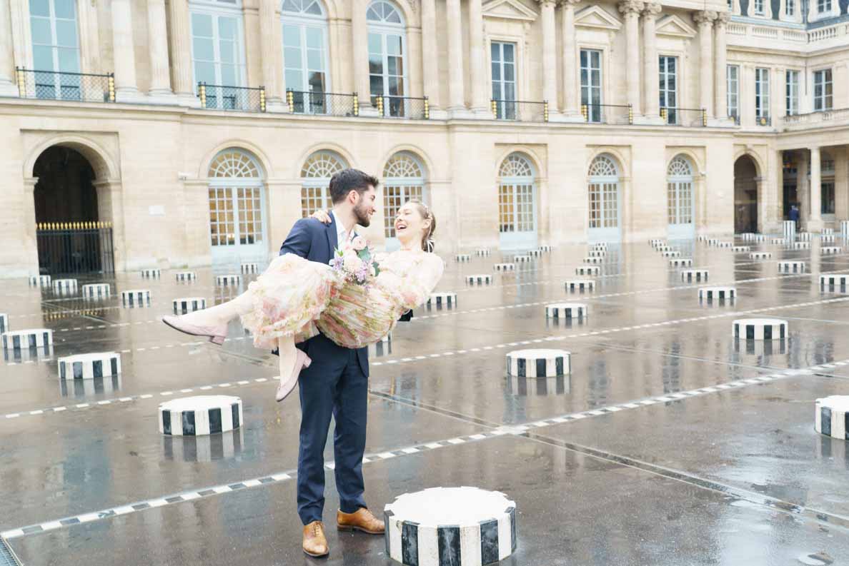 photo du mariage à Paris Palais Royal, marié porte la mariée dans ses bras sous les colonnes de Buren après la pluie.
