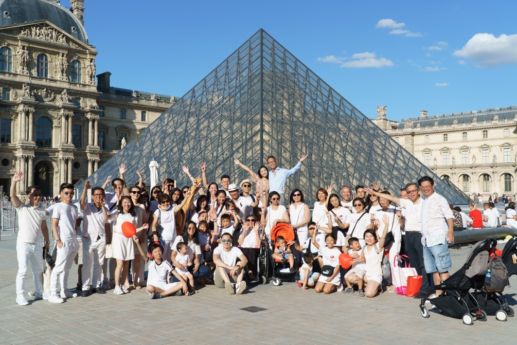 Surprise marriage proposal at the Louvre Pyramid, group photo with the couple and their family on a sunny afternoon